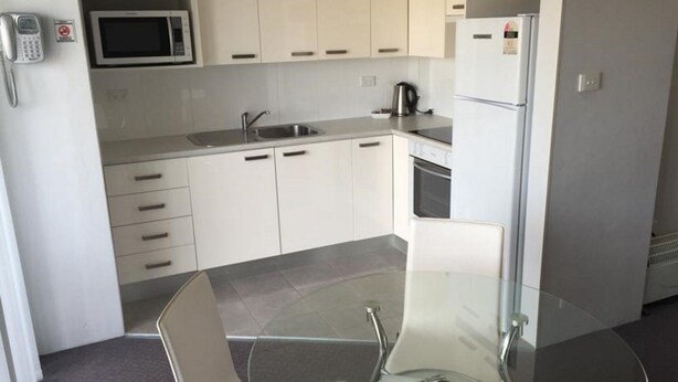A modern kitchen with white cabinets, a microwave, a refrigerator, a kettle, and a glass table. - Mollymook Aquarius Apartments (Mollymook)