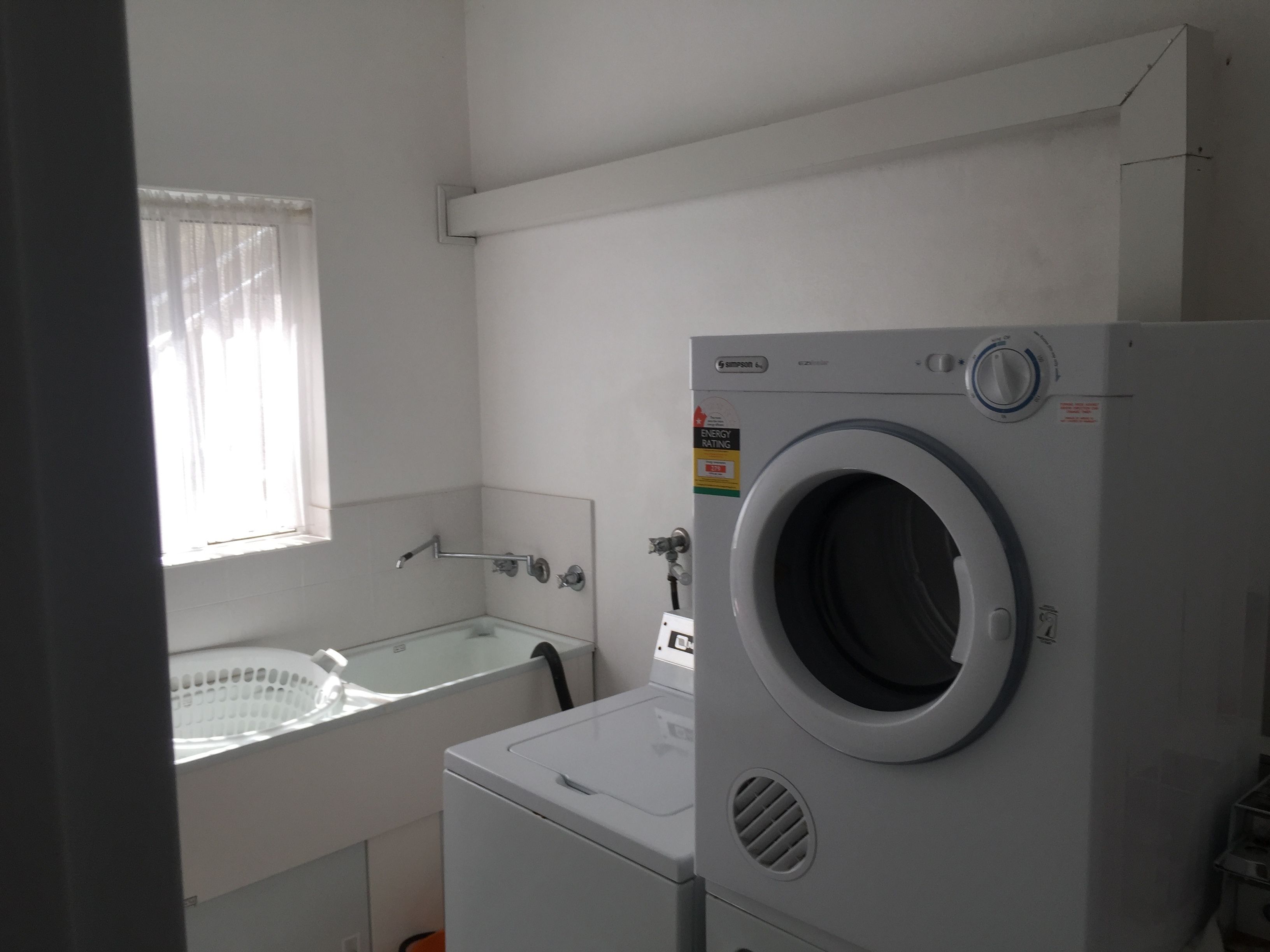 A laundry room with a front-loading washer and dryer, a sink, and a window with sheer curtains.