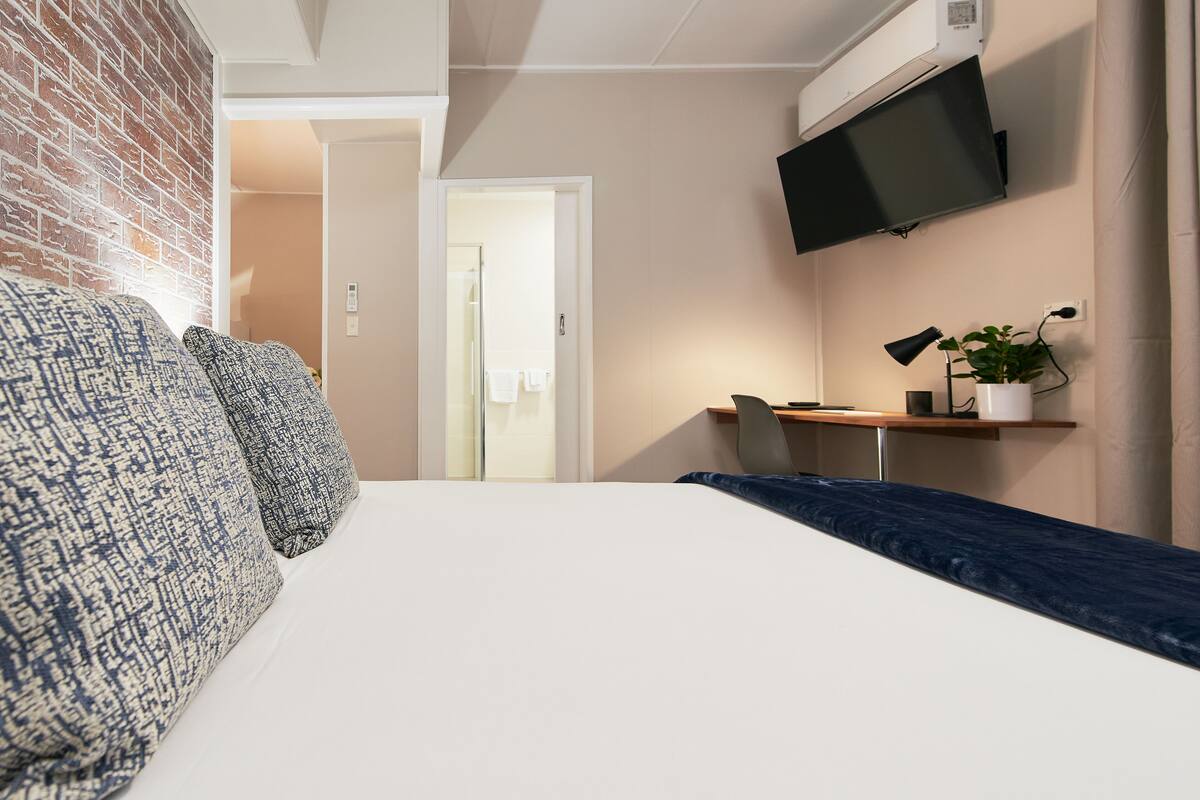 Una habitación de hotel moderna con cama, escritorio, televisor y una planta en maceta.