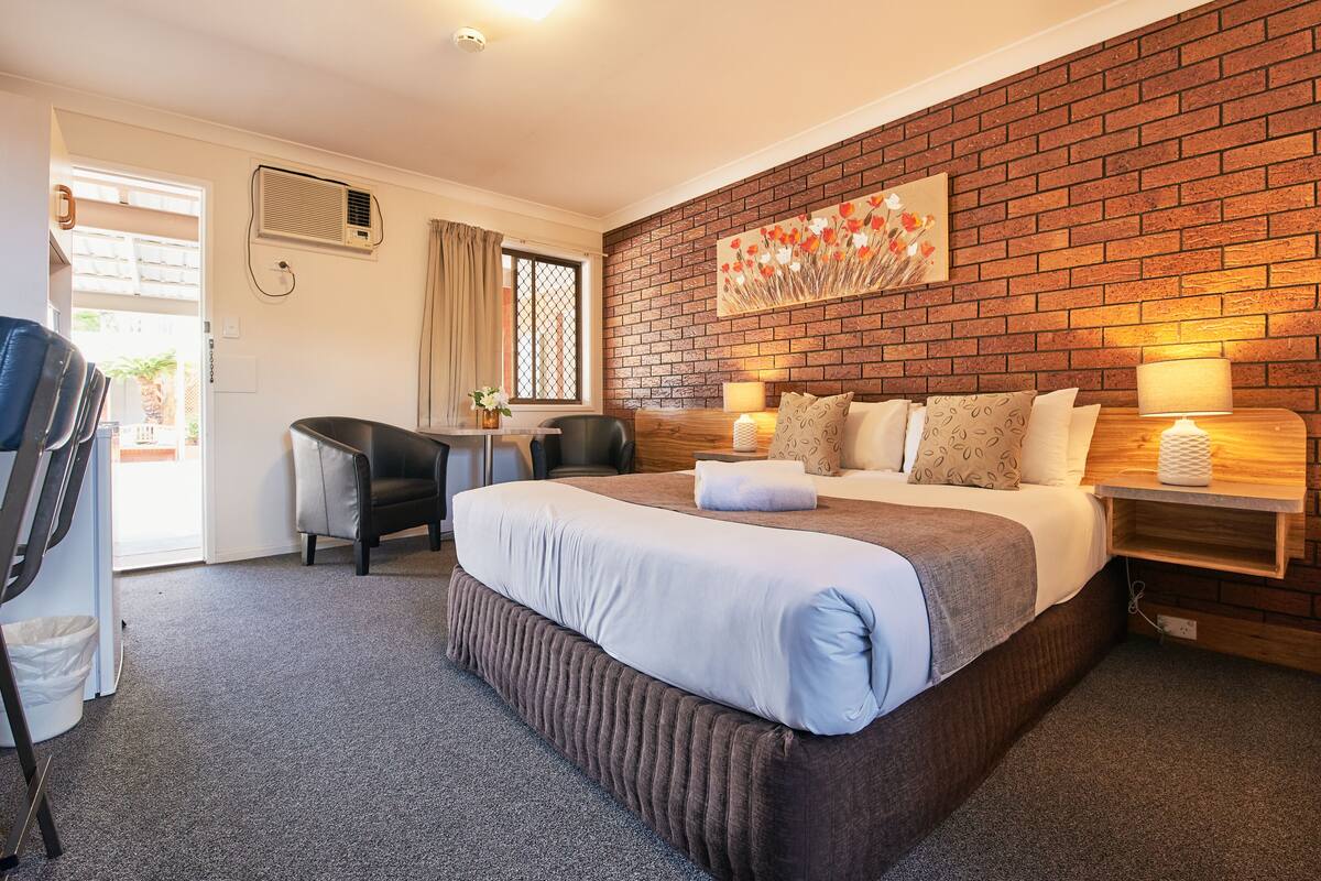 Habitación de hotel con una cama grande, un escritorio, una silla, una pared de ladrillo y una ventana con cortinas.
