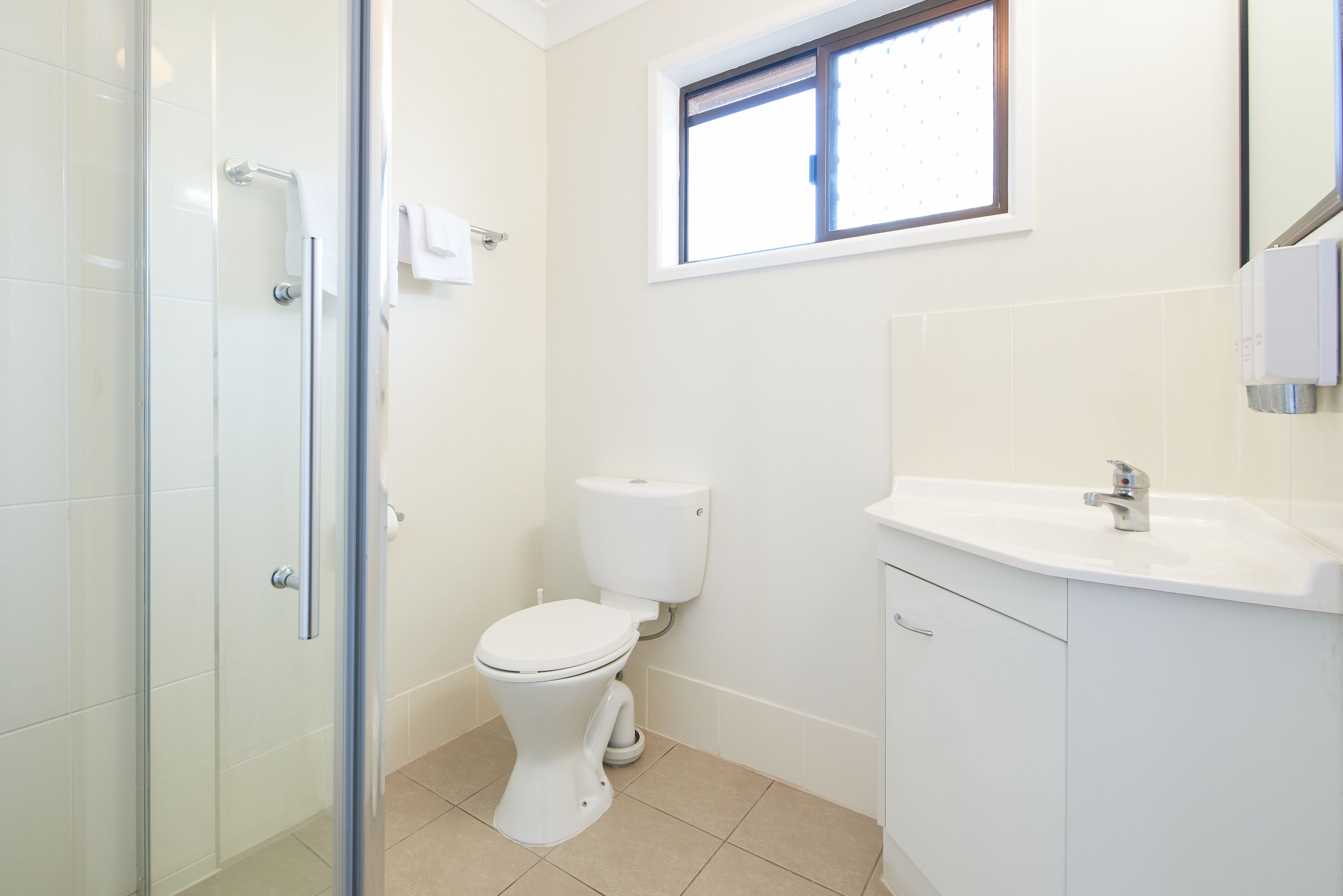 Un baño con cabina de ducha de vidrio, inodoro y lavamanos con espejo.