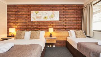 Two beds with matching bedding and patterned pillows, each with a bedside table and lamp.