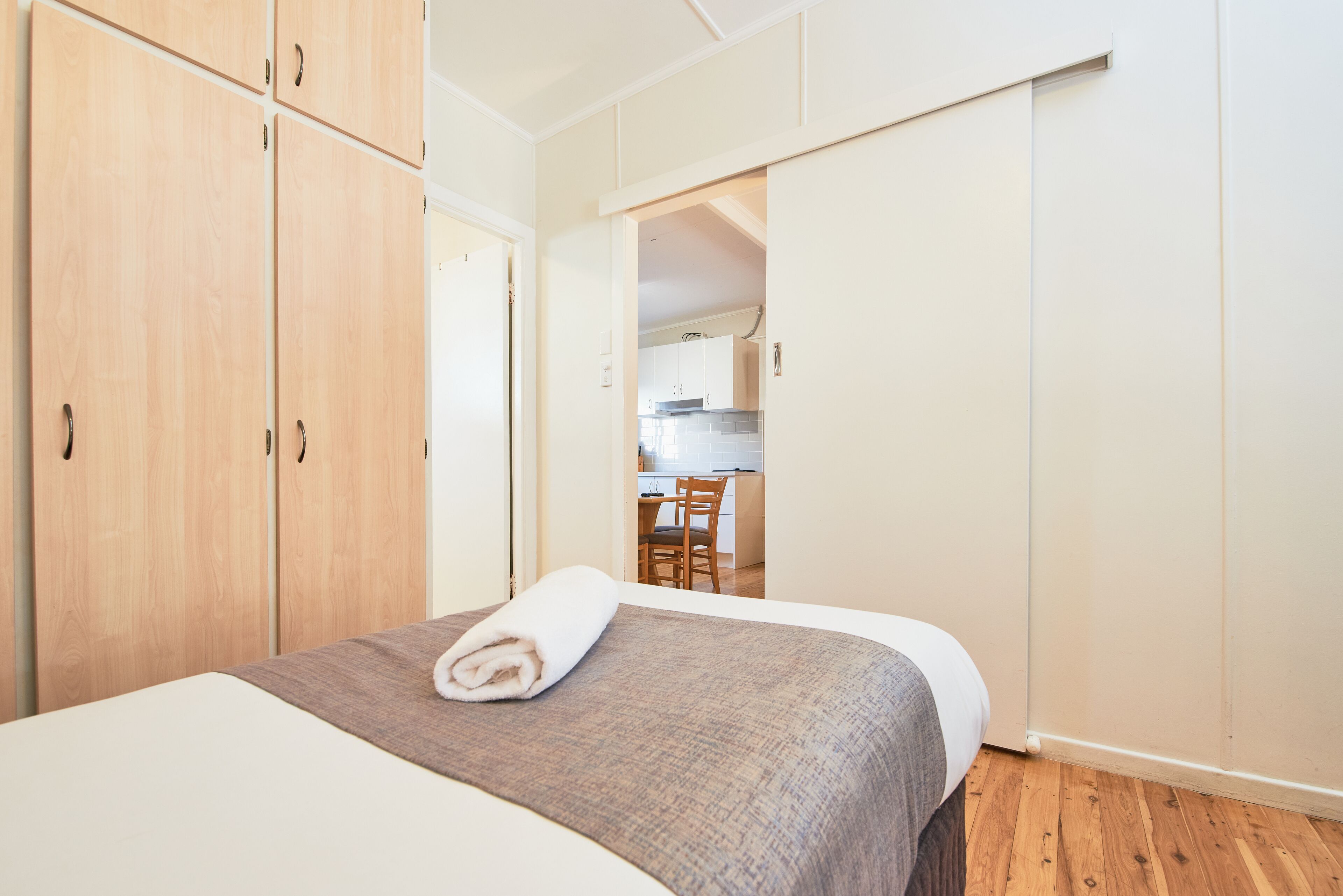 Un dormitorio con cama, armario de madera y puerta abierta que da a una cocina.