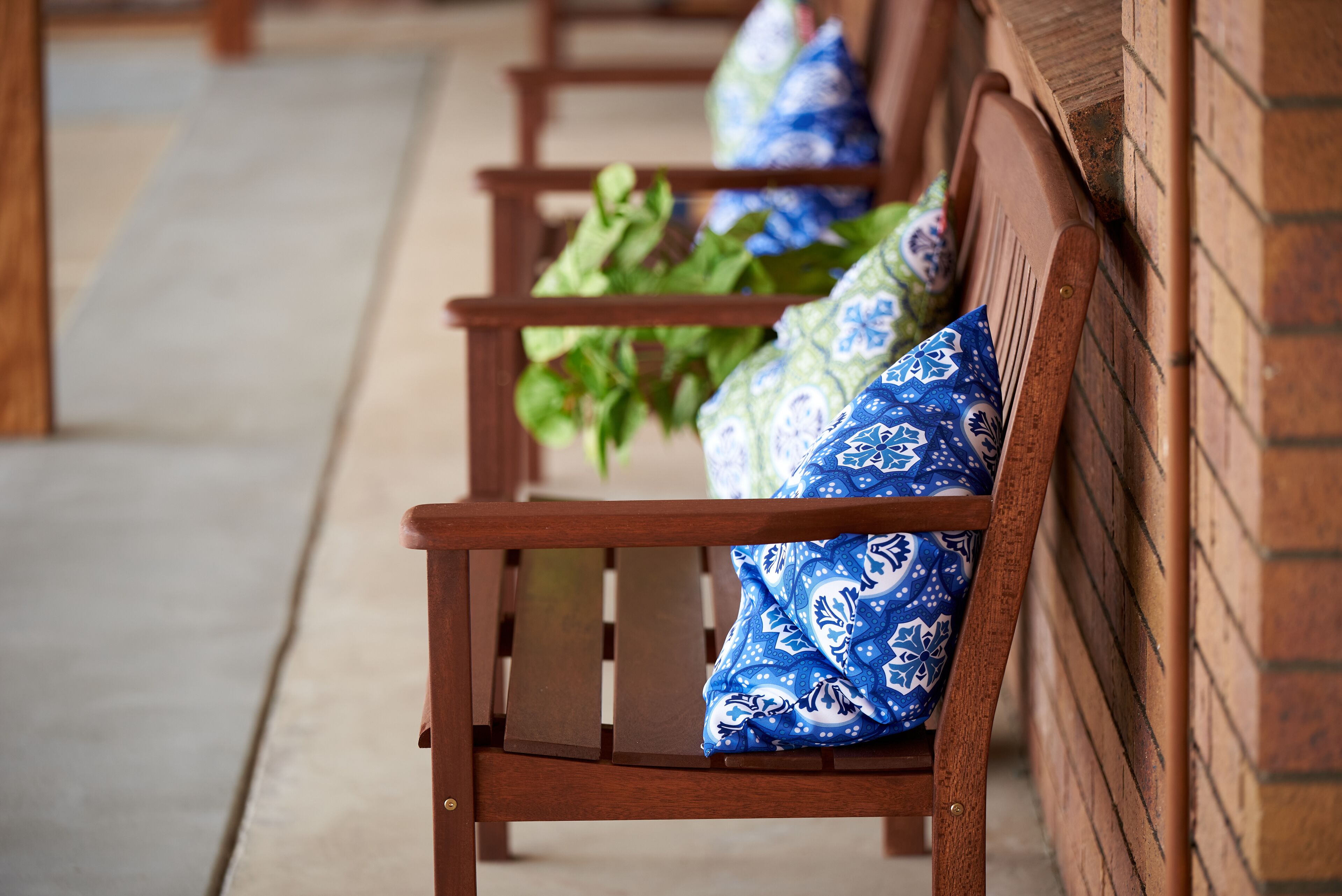 A row of wooden benches with patterned cushions against a brick wall.