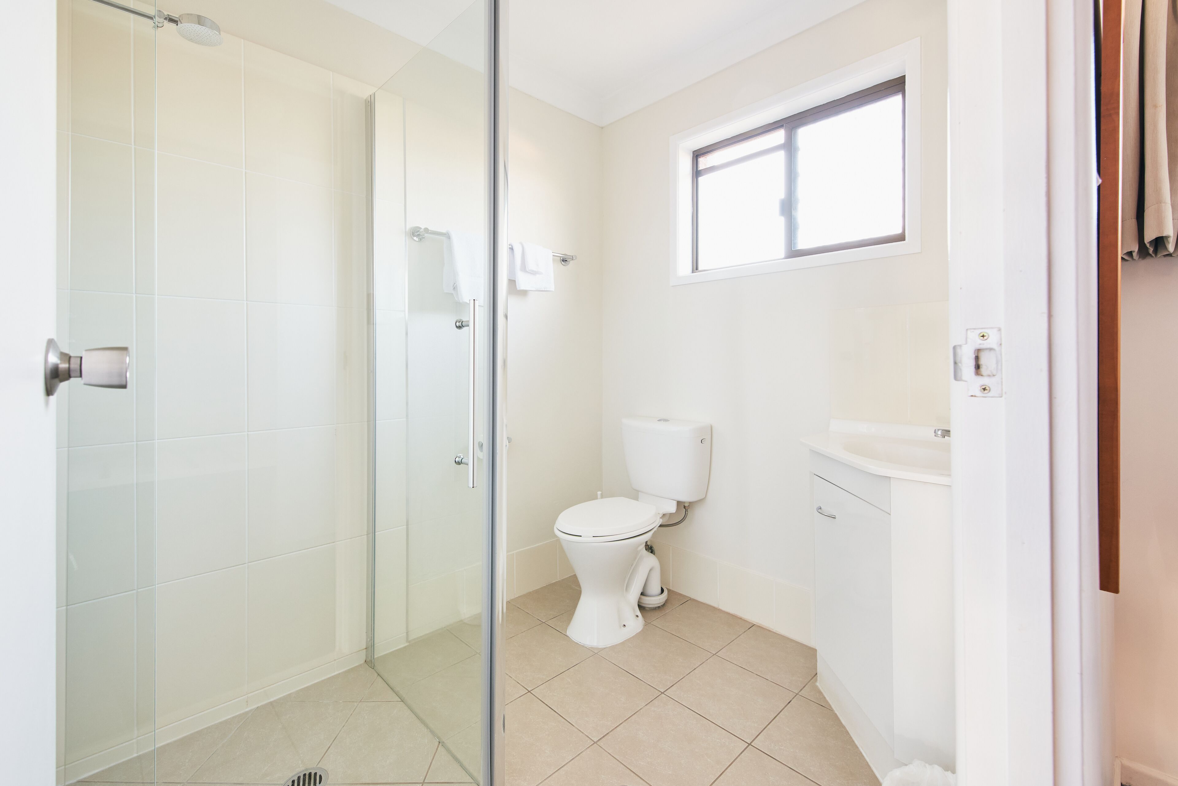 A bathroom with a glass shower enclosure, a toilet, and a sink.