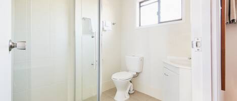 A bathroom with a glass shower enclosure, a toilet, and a sink.