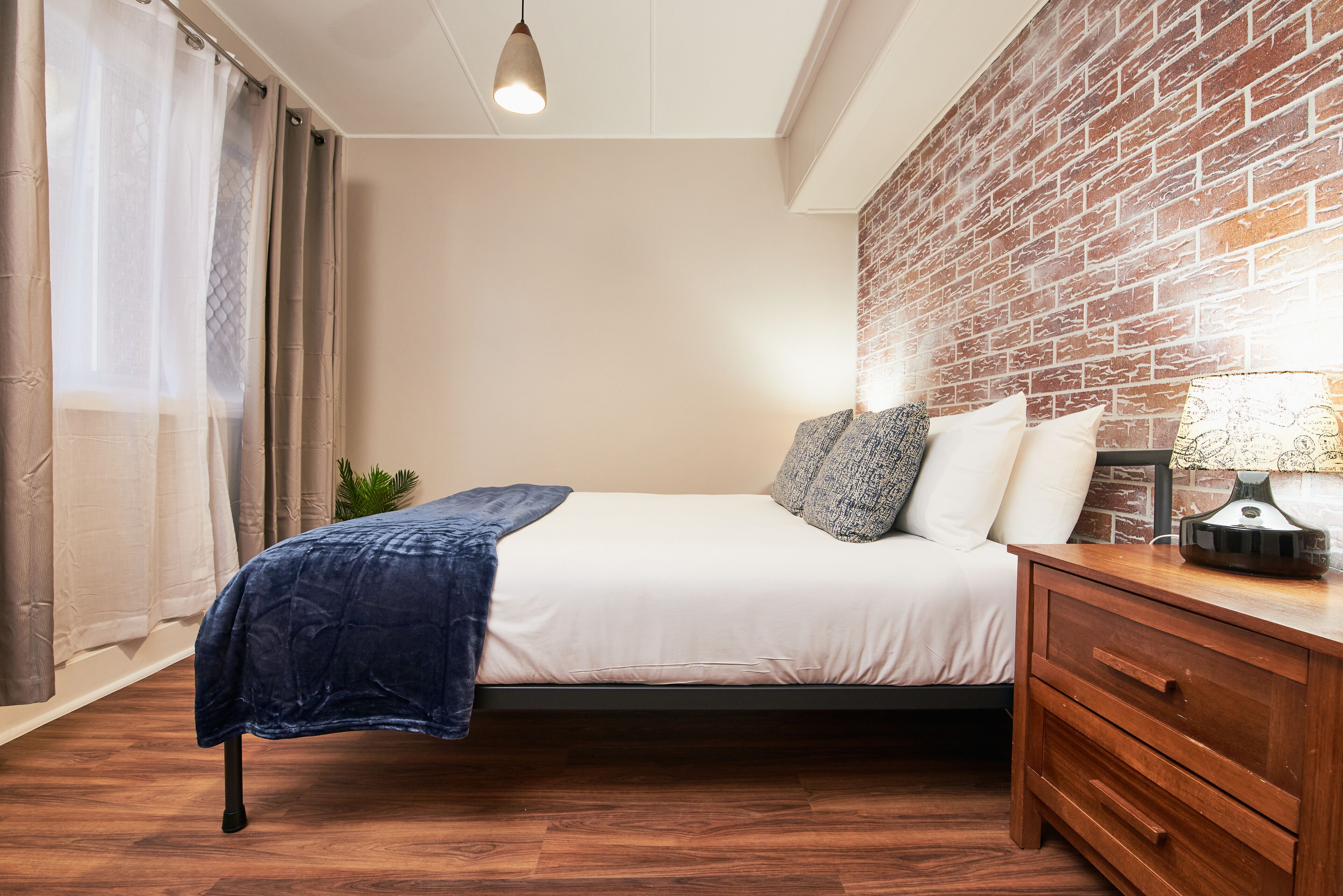 A bedroom with a bed, wooden nightstand, and a brick wall.