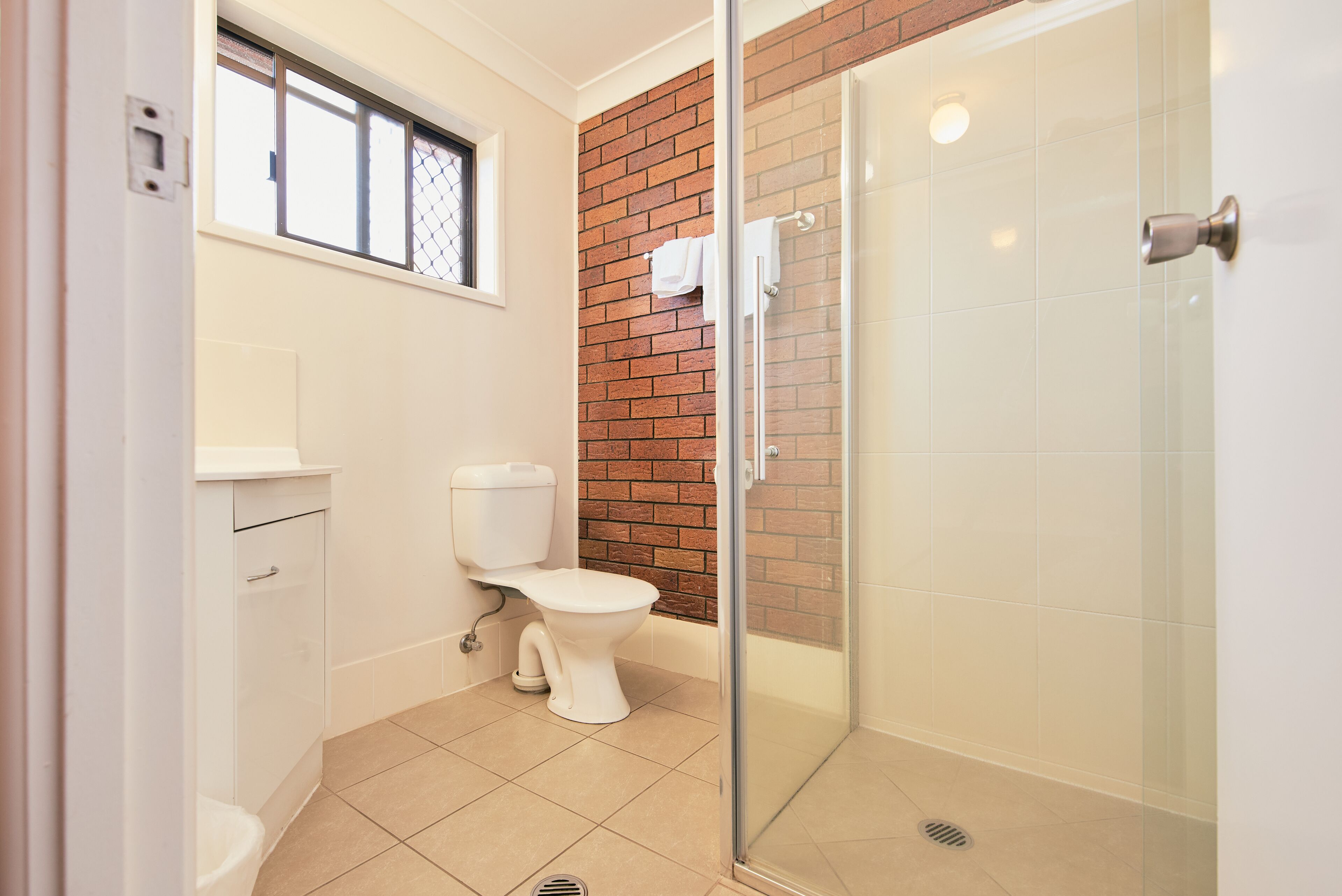 A bathroom with a toilet, a glass-enclosed shower, and a window with a metal screen.