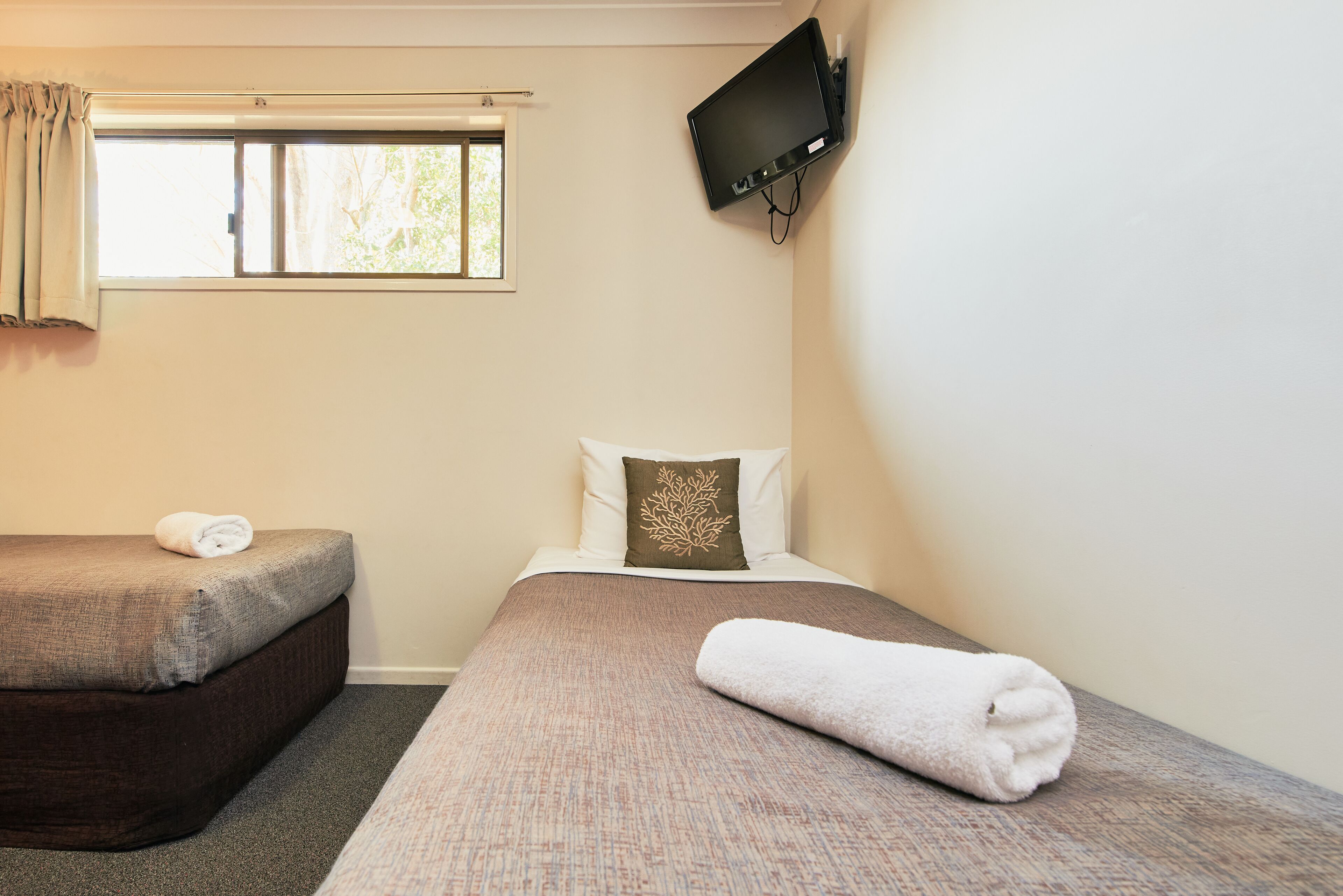 A hotel room with two beds, a TV mounted on the wall, and a window with curtains.