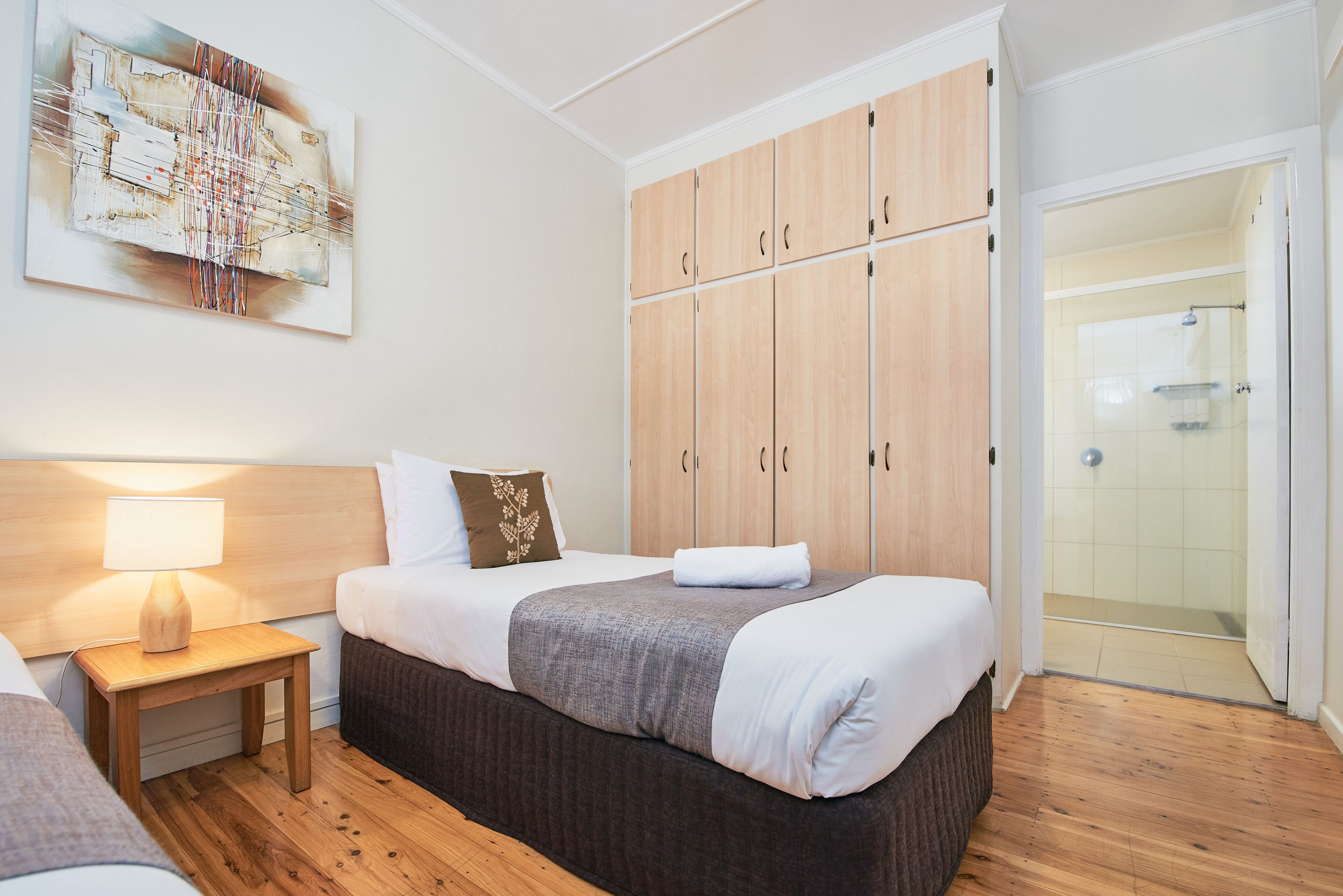 Une chambre d’hôtel comprenant un lit, une table de chevet, une armoire en bois et un espace douche.