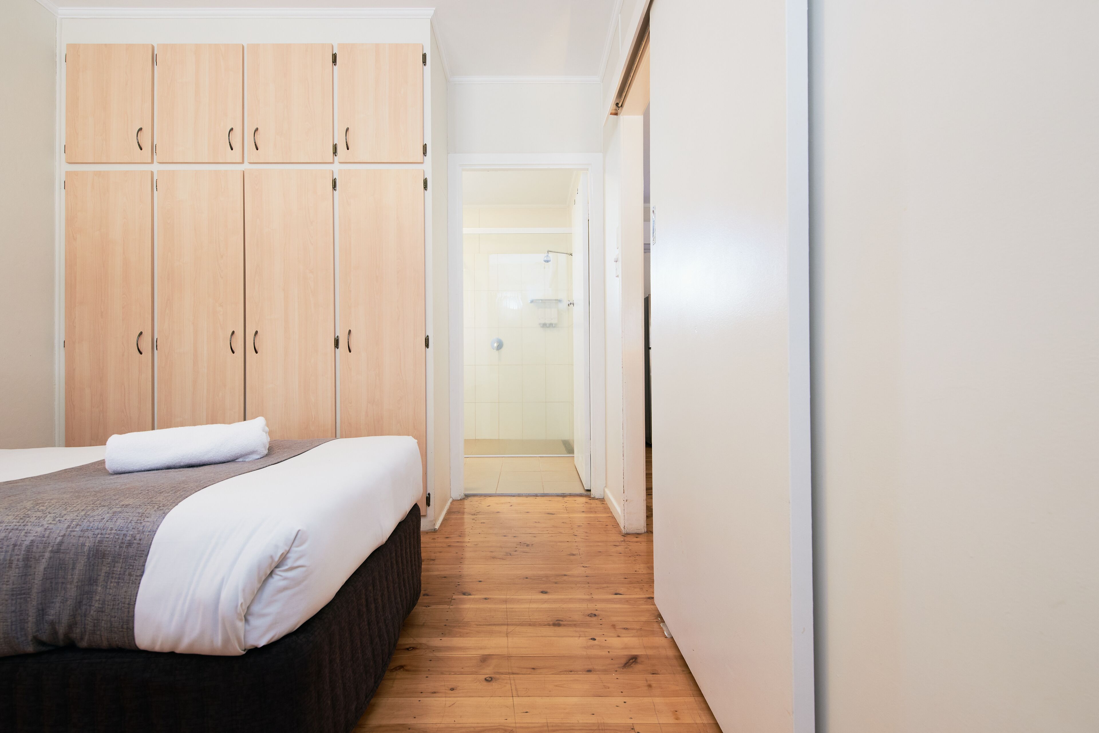 A bedroom with a bed, wooden wardrobe, and a bathroom visible through an open door.
