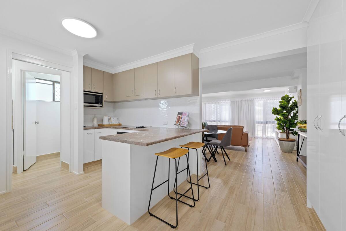 A modern kitchen with a central island, bar stools, and a dining area with a table and chairs.