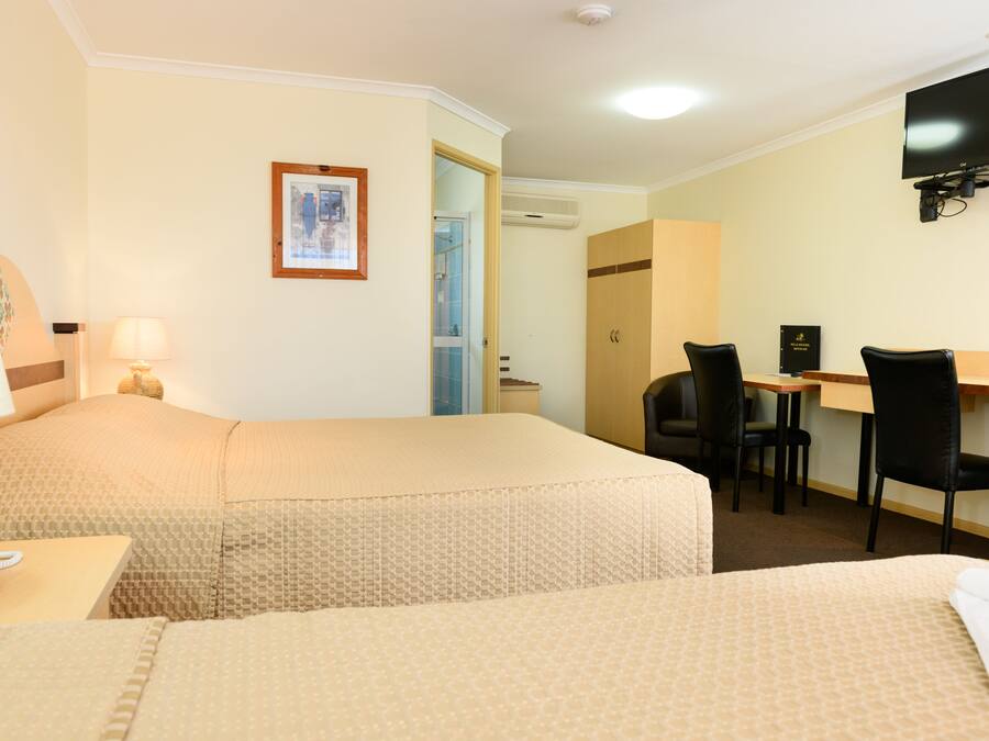 A hotel room with two beds, a desk with a chair, a television, and a framed picture on the wall.