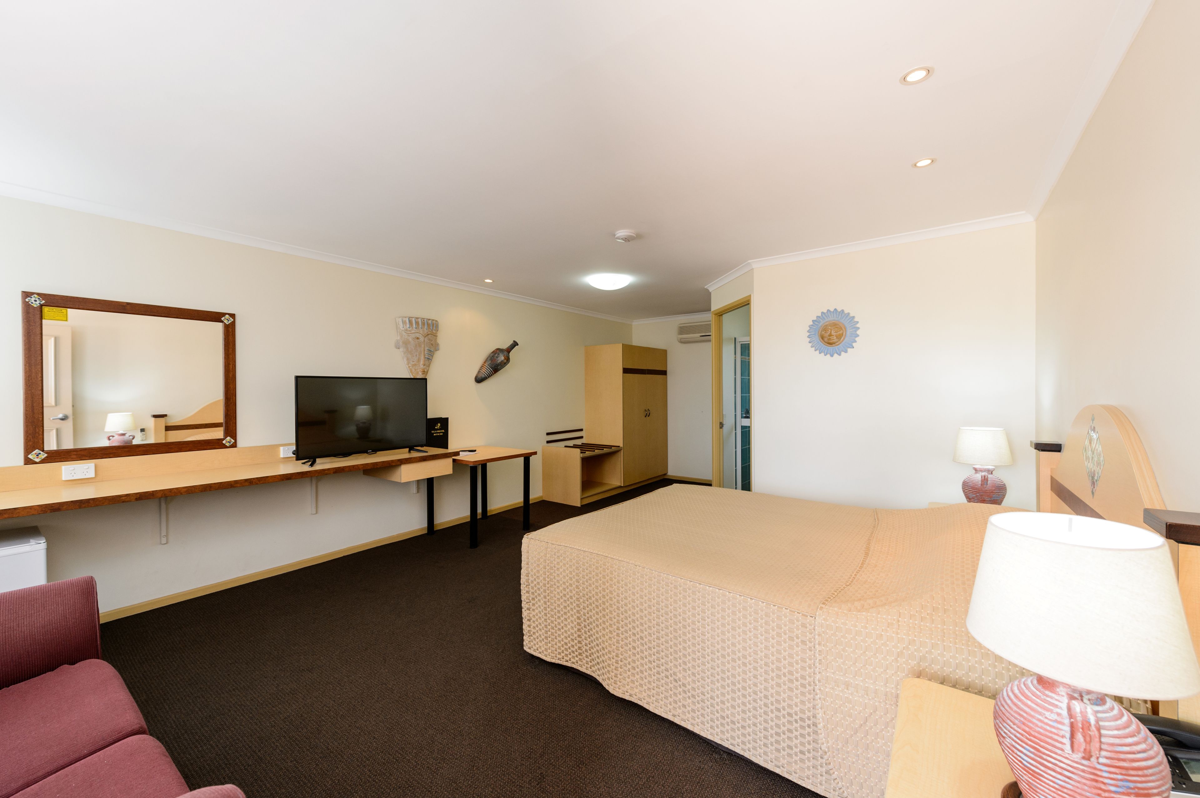 Ein Hotelzimmer mit einem Bett, einem Schreibtisch mit Fernseher, einem Sessel, einer Lampe und einem kleinen Tisch.