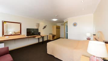 Ein Hotelzimmer mit einem Bett, einem Schreibtisch mit Fernseher, einem Sessel, einer Lampe und einem kleinen Tisch.