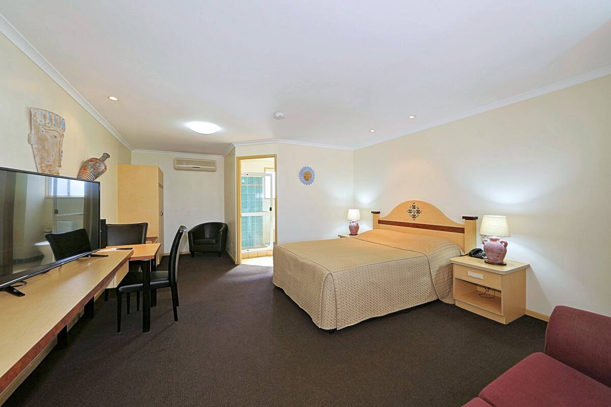 A hotel room with a bed, bedside tables, a desk with a chair, a television, and a door leading to a bathroom.