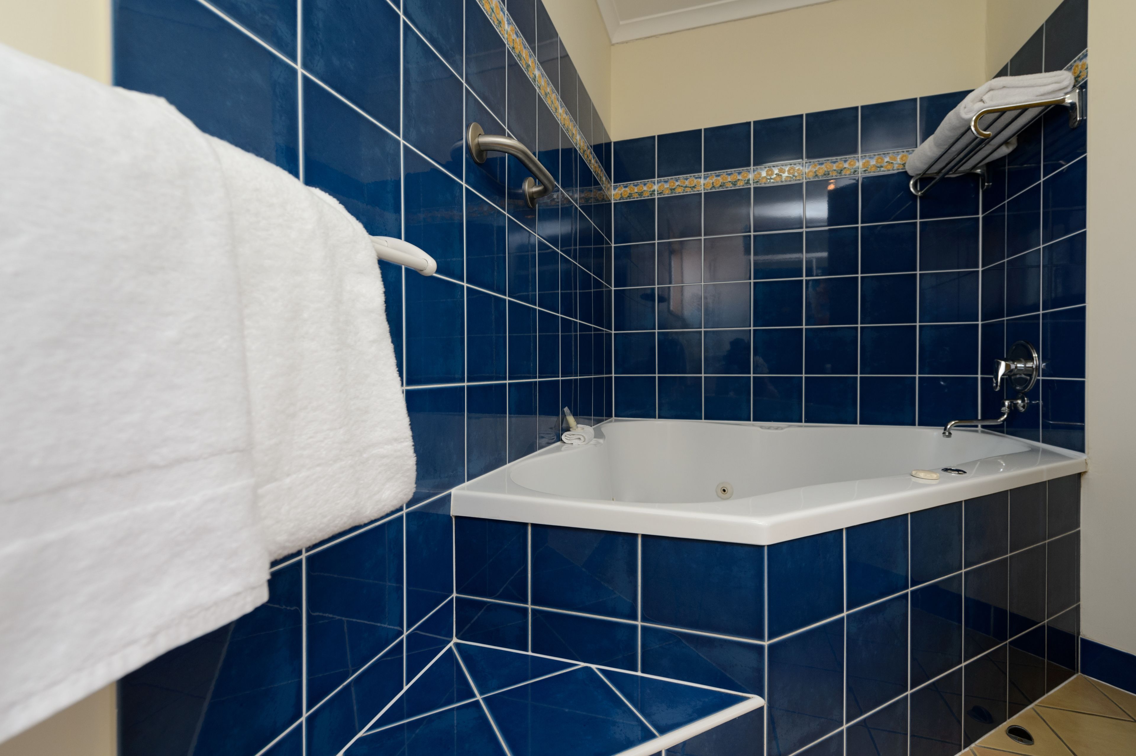 A bathroom with a white bathtub, blue tiles, a towel rack, and a shower head.
