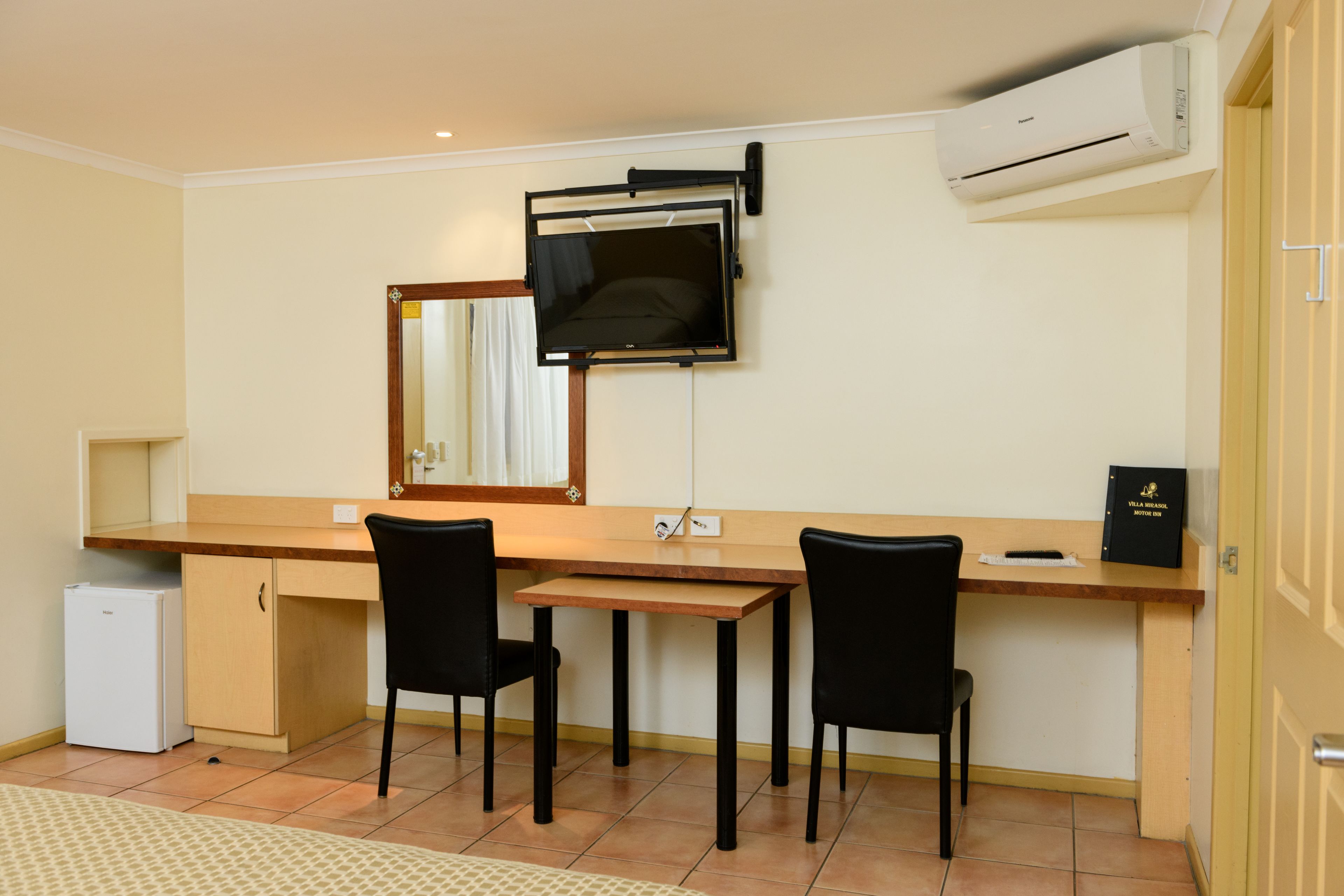 A small kitchenette with a refrigerator, a wooden countertop, and two black chairs.
