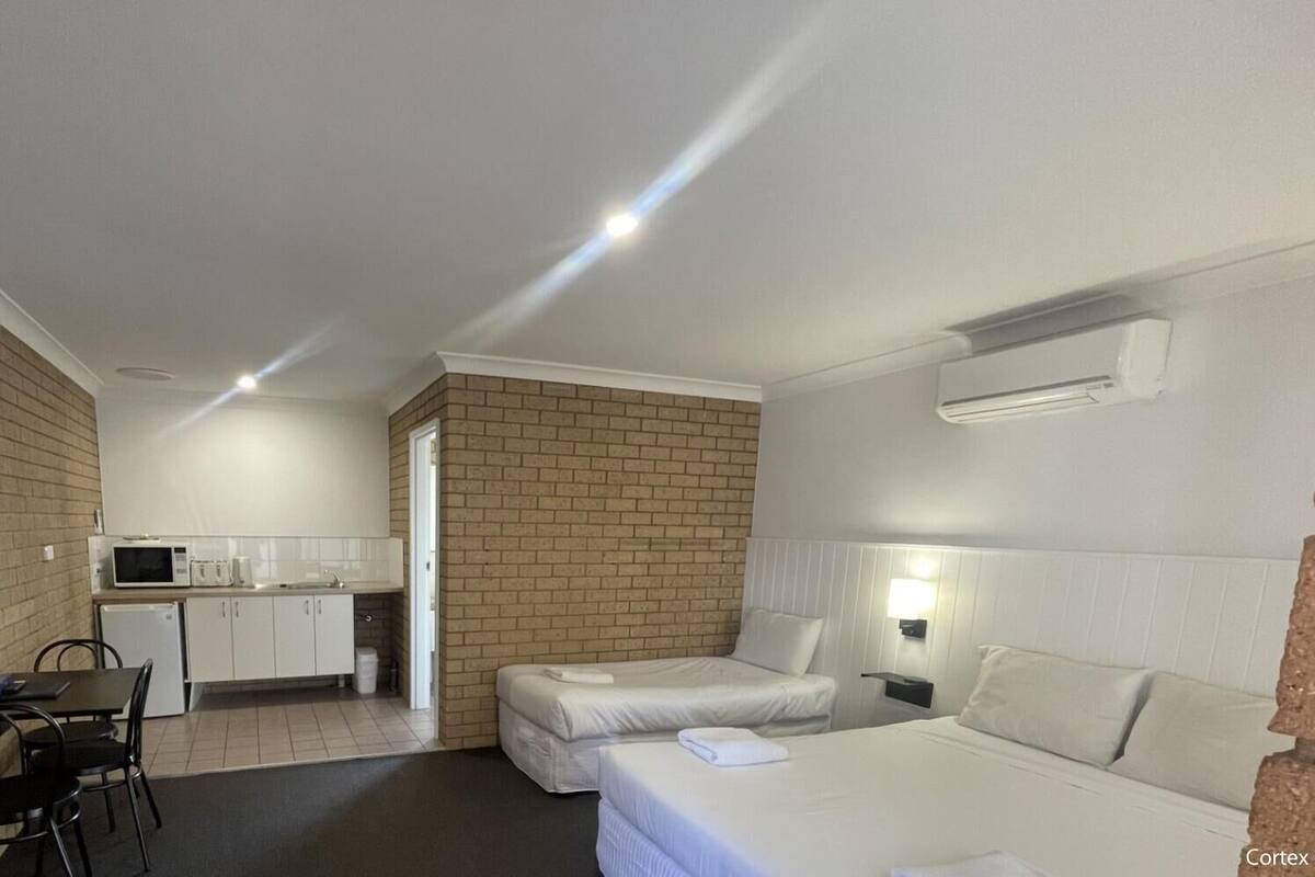 Ett kompakt hotellrum med ett litet kök, en säng, ett skrivbord och en TV.