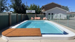 Ein rechteckiger Pool mit einer Holzdielen-Terrasse im Vordergrund, umgeben von einem grünen Zaun und einem Schild für das Allawa Motor Inn im Hintergrund.