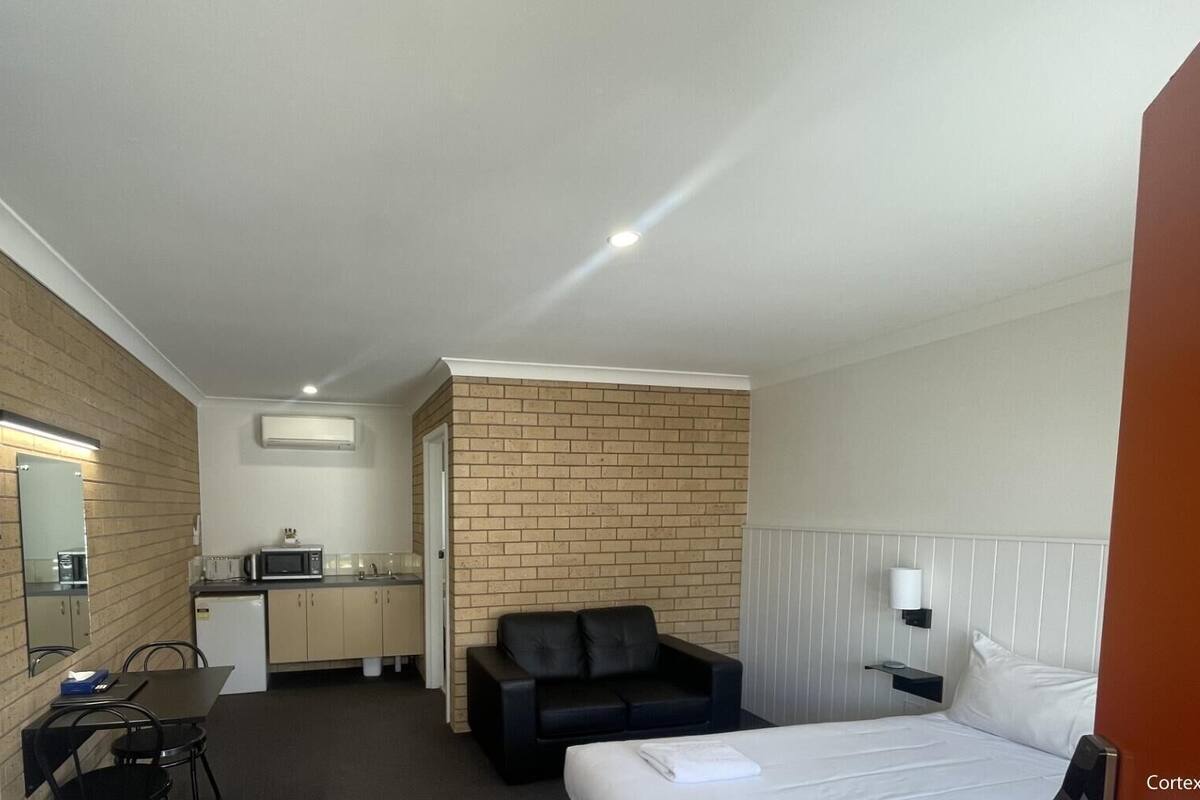 Ett kompakt hotellrum med en säng, ett litet skrivbord med en stol, ett litet pentry och en vägg som är accentuerad med tegelstenar.