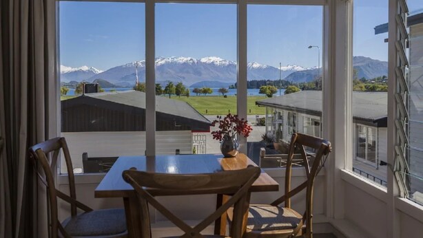 Uma área de refeições com mesa e cadeiras, um vaso com flores e vista para montanhas e um lago.