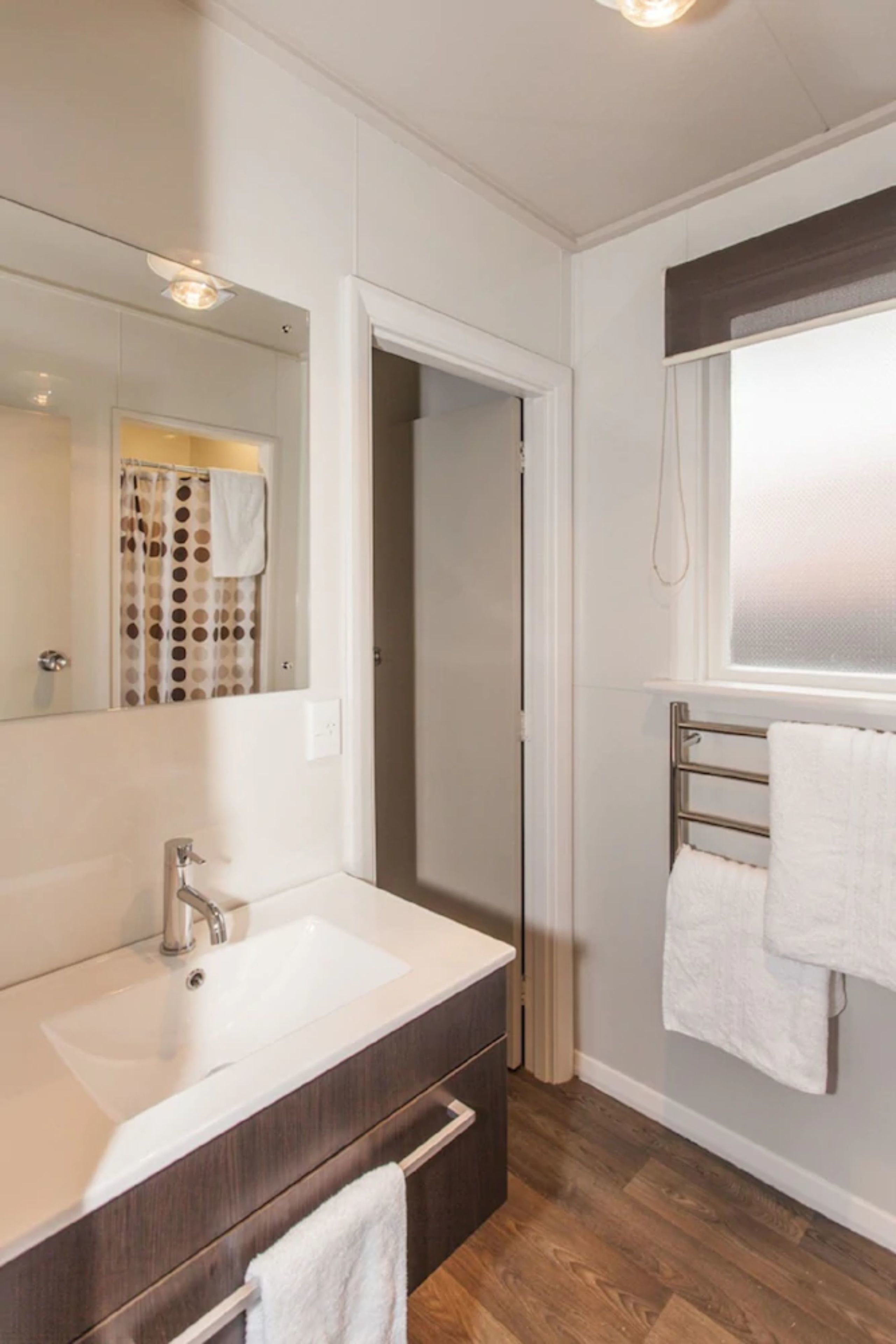 Une salle de bain moderne avec un grand miroir, un lavabo blanc et un porte-serviettes.