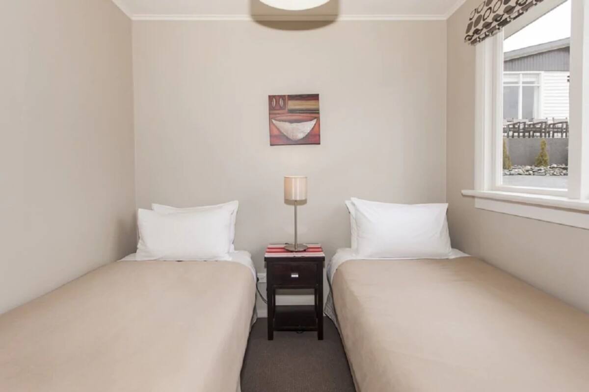 A twin bedroom with two beds, a nightstand, a lamp, and a painting on the wall.