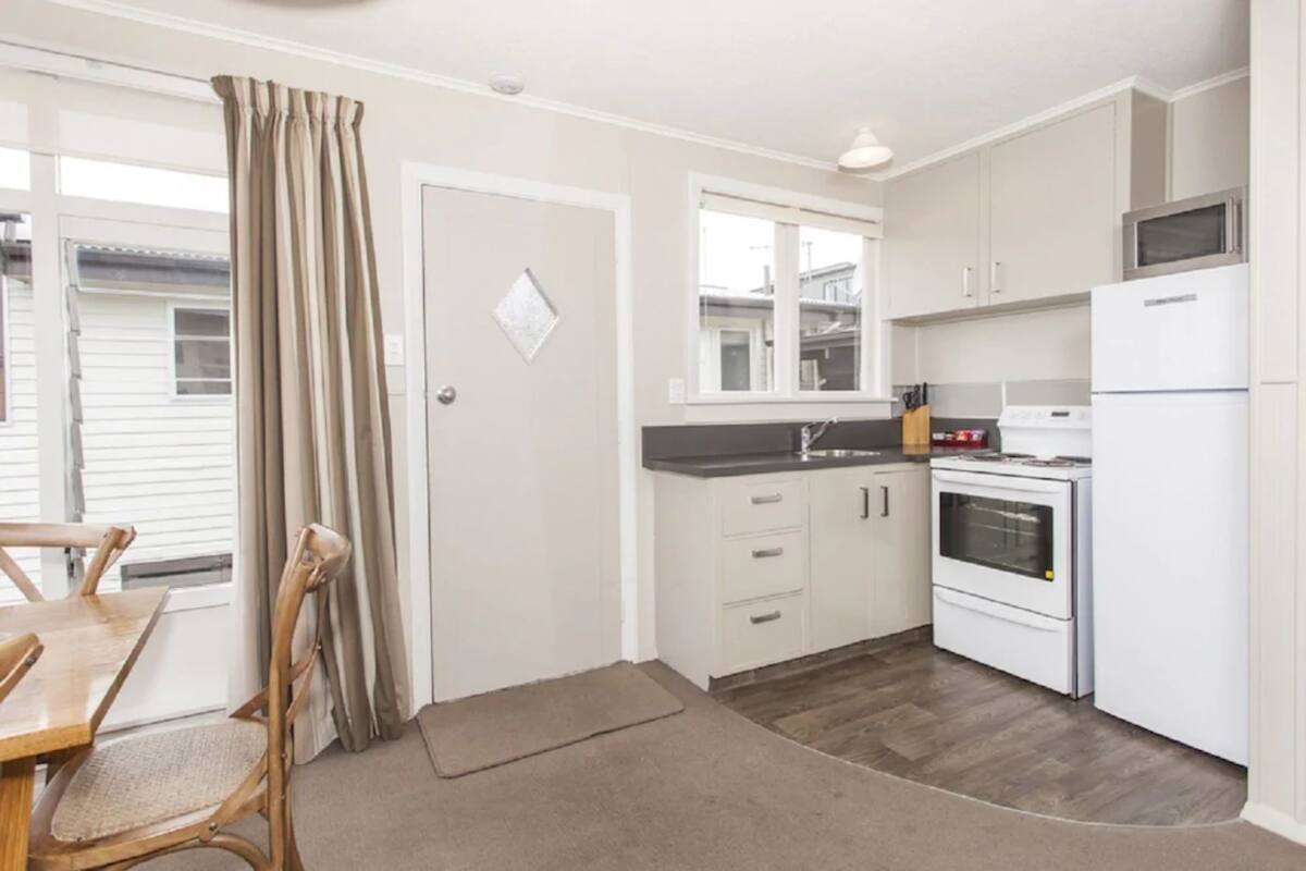 A compact kitchen with white cabinets, a microwave, and a stove. There is a dining area with a wooden table and chairs.