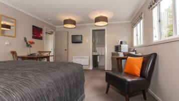 A hotel room with a bed, a desk, a chair with an orange cushion, a television, and a window with a view.