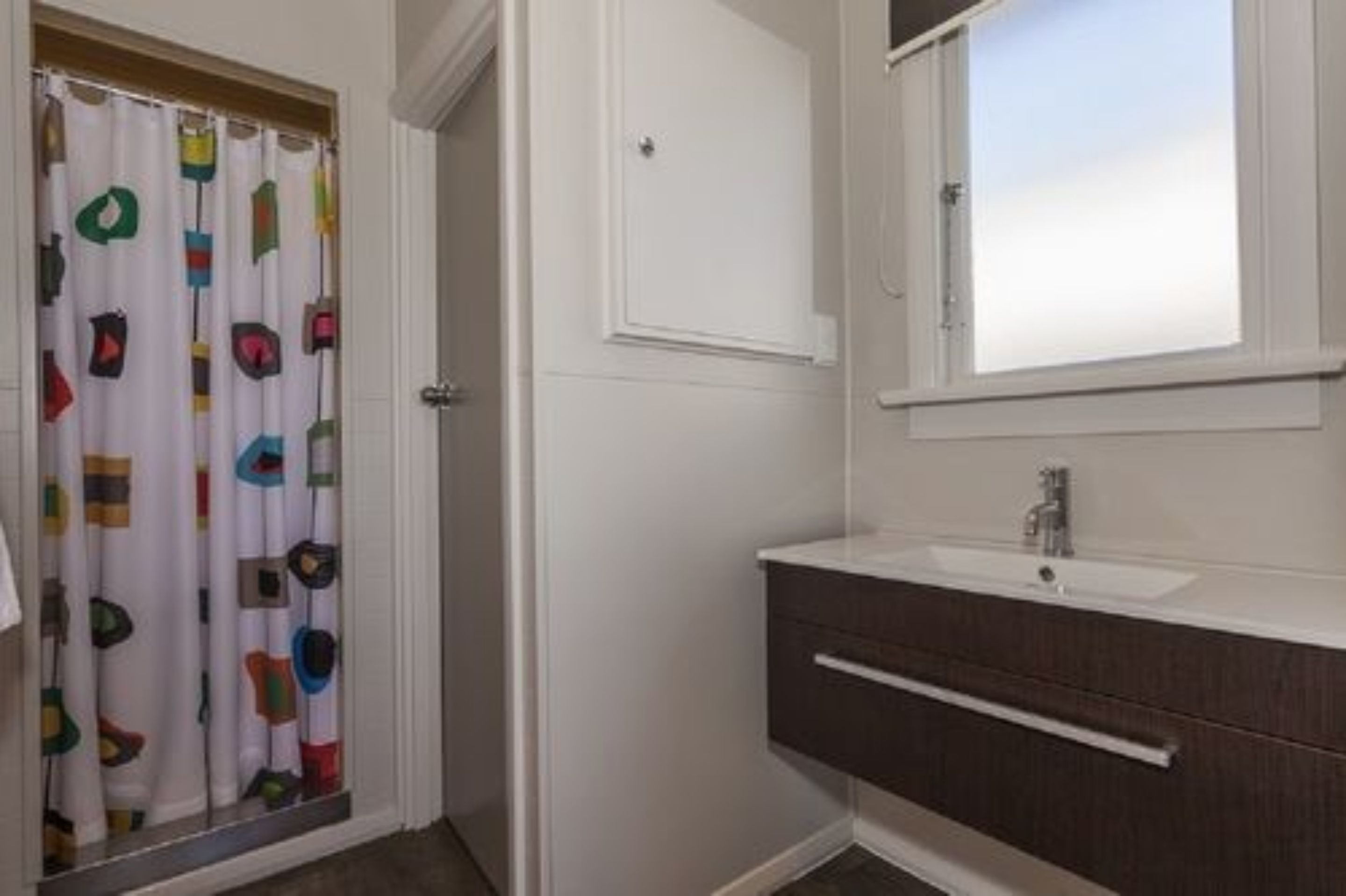 A bathroom with a white sink, dark wooden cabinet, and a shower curtain with colorful patterns.