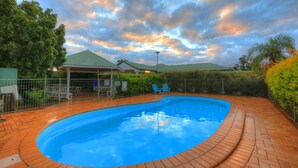 A swimming pool with a brick deck, surrounded by a fence and trees. - Jacaranda Country Motel (St. George)