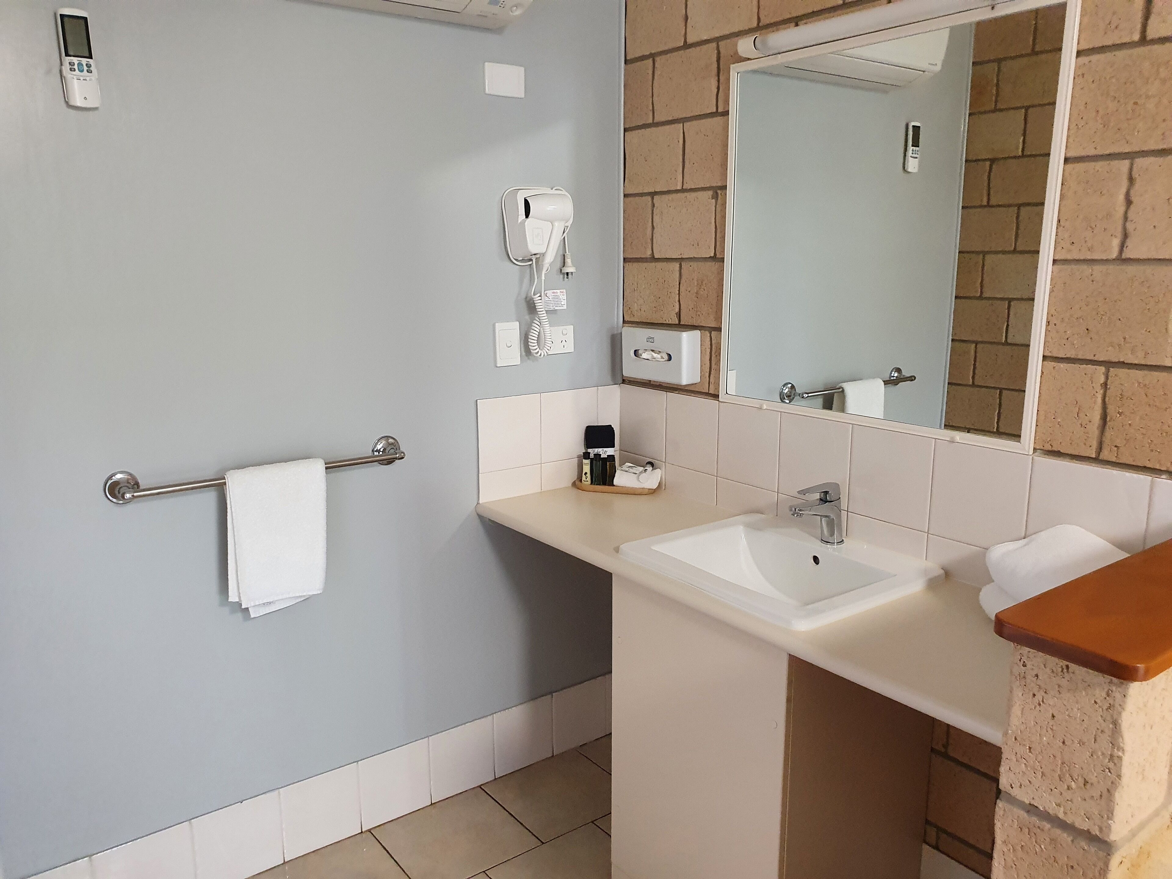 A bathroom with a sink, mirror, towel rack, and a hairdryer on the wall.