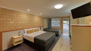 A hotel room with two beds, a TV, a small desk, and a window with curtains.