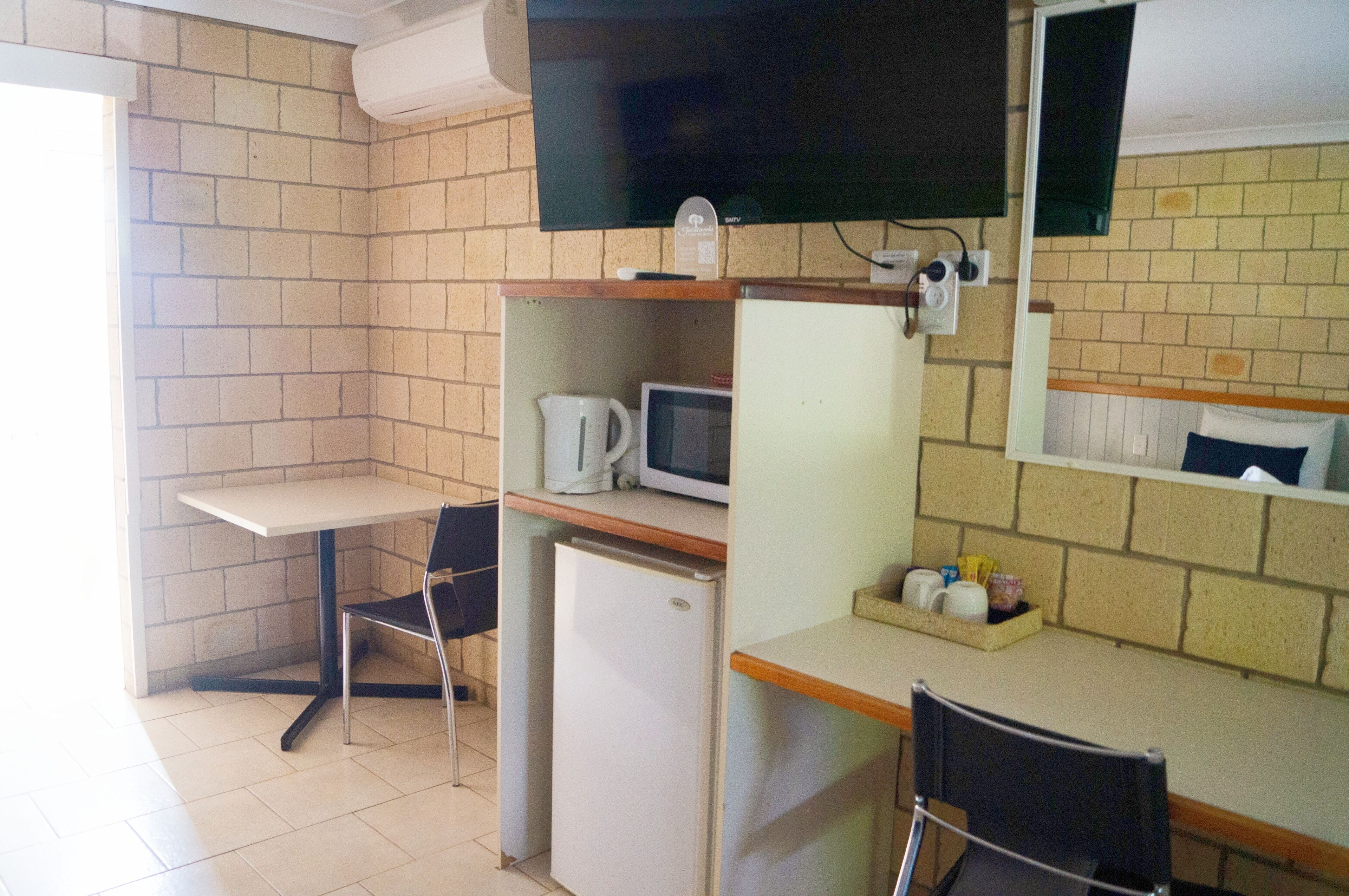 Une petite cuisine équipée d’un four à micro-ondes, d’une machine à café et d’un réfrigérateur. On y trouve également une table et deux chaises.