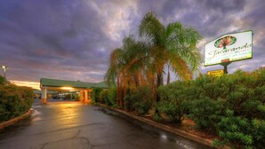 A motel entrance with a covered parking area, palm trees, and a sign indicating wireless internet availability. - Jacaranda Country Motel (St. George)