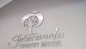 A wall sign for Jacaranda Country Motel with a tree logo, a wicker basket with towels, and a wooden box with a bag of laundry detergent. - Jacaranda Country Motel (St. George)
