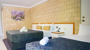 A hotel room with two beds, a brick wall, and a painting of a road with trees. - Jacaranda Country Motel (St. George)