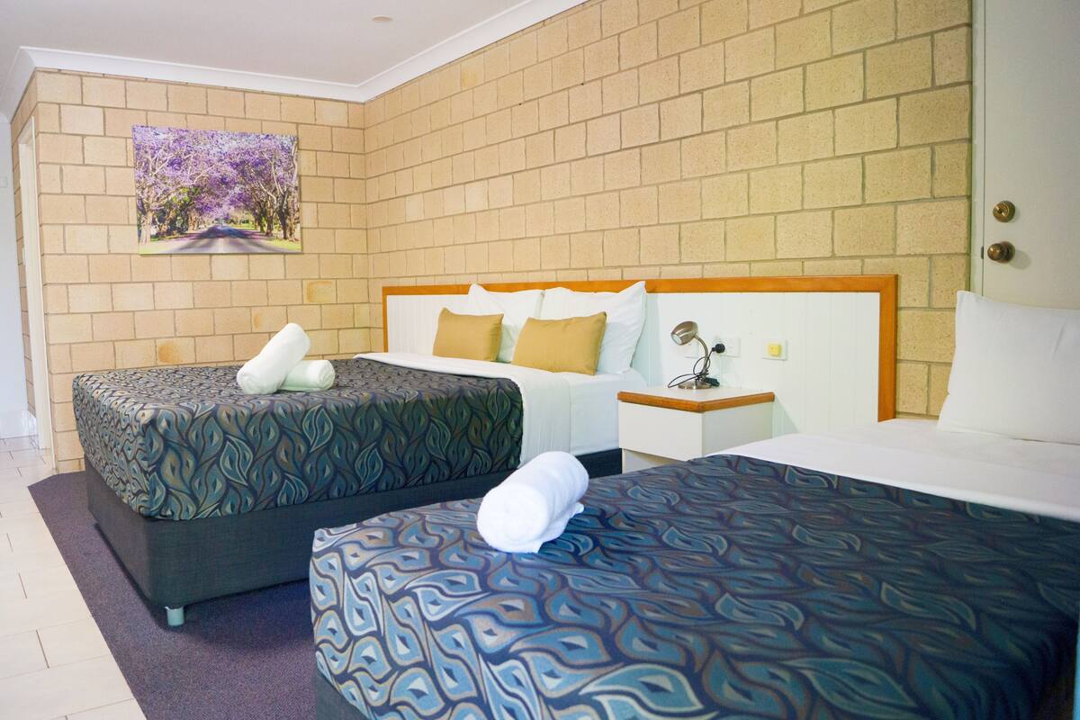A hotel room with two beds, a brick wall, and a painting of a road with trees.