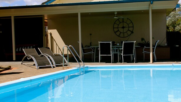 Une piscine avec des chaises longues et une table placées sous un espace abrité.