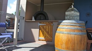 Un espace extérieur aménagé en terrasse, avec un four à pizza au feu de bois, une lanterne décorative et un tonneau en bois.