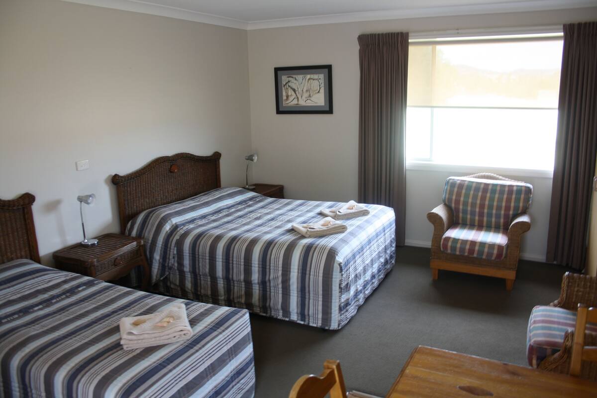 A hotel room with two beds, a chair, a table, and a window with curtains.