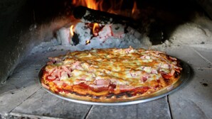 Une pizza cuite dans un four à bois, où l’on peut voir les flammes.