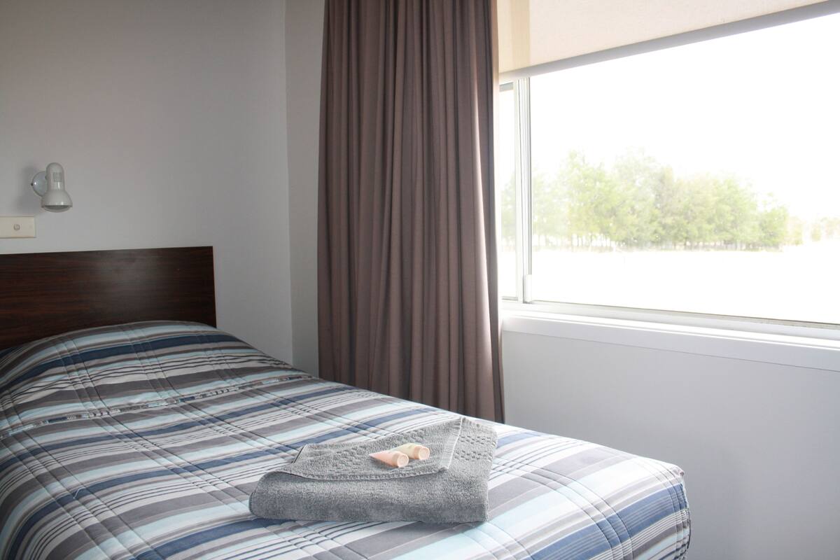 A bed with a striped bedspread, a grey blanket, and a pair of slippers.