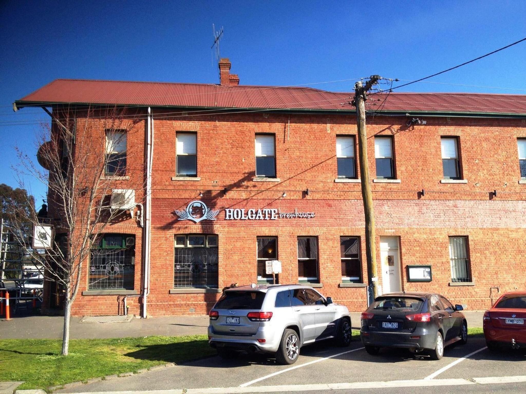 Un bâtiment en briques rouges sur lequel on peut lire l’inscription « HOLGATE, brasserie ». Trois voitures sont garées devant.