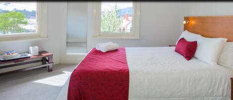 Habitación de hotel con cama, mesita de noche, ventana y vistas al exterior.