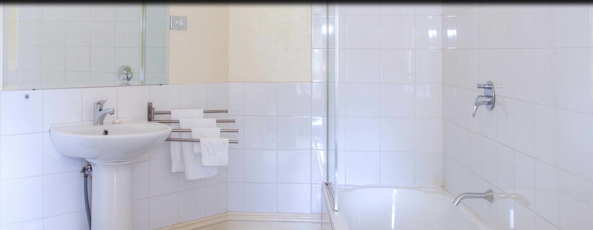 A bathroom with a sink, mirror, towel rack, and a shower area.
