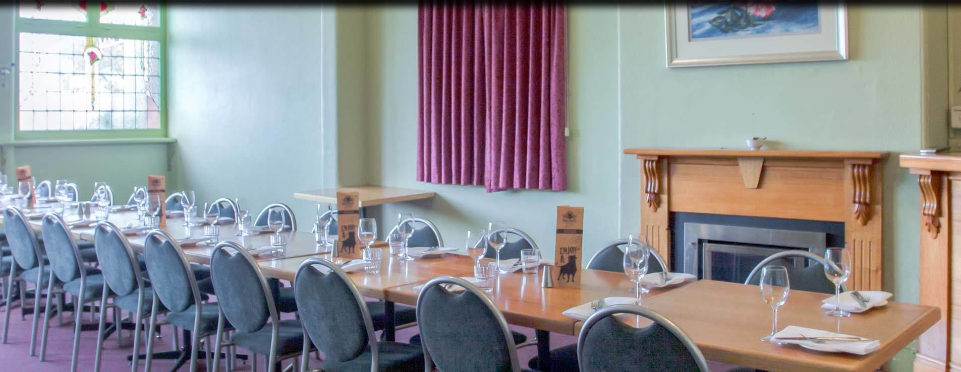 A dining room with a long table set for a meal, chairs, a fireplace, and a window with curtains.