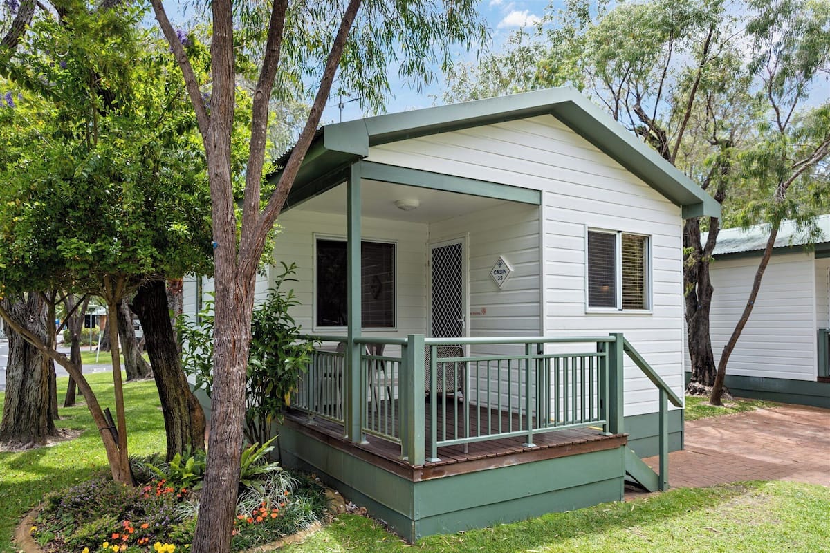 A small, single-story cabin with a porch and a fenced deck area.