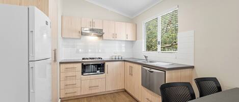 A modern kitchen with wooden cabinets, a built-in oven, a dishwasher, and a window with blinds.